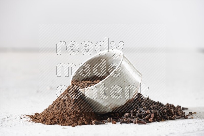 A beige ceramic bowl with cloves powder spilled out of it on a textured white flooring