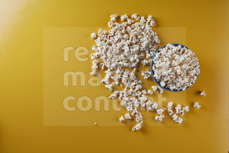 A blue pottery bowl full of popcorn with popcorn beside it on a yellow background in different angles