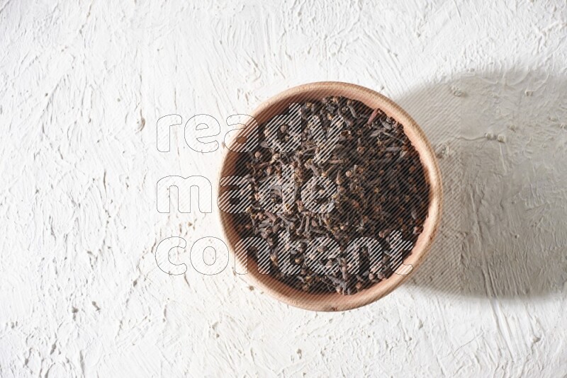 A wooden bowl full of cloves on a white flooring