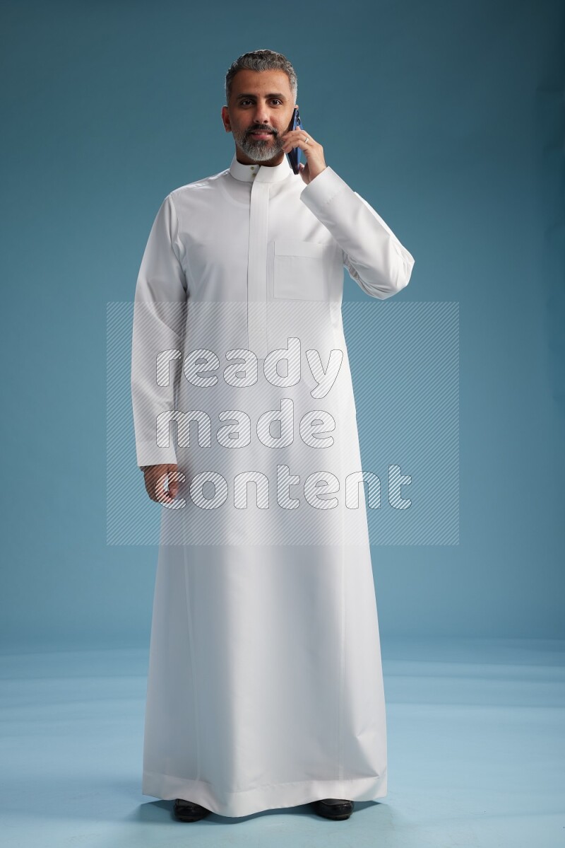 Saudi man wearing thob talking on the phone on blue background
