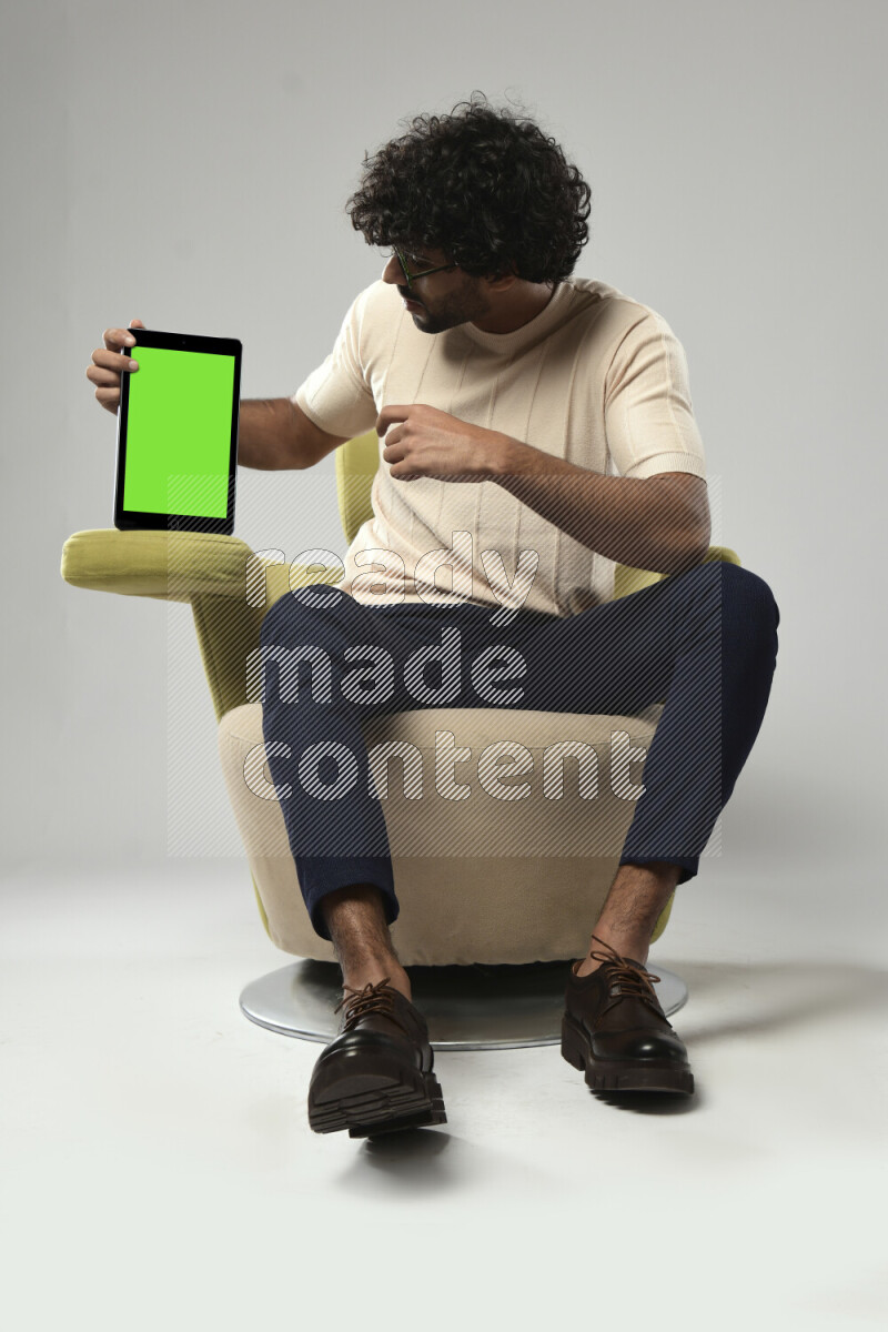 A man wearing casual sitting on a chair showing a tablet screen on white background