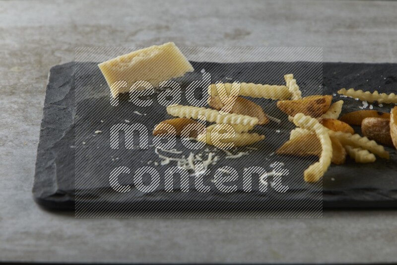 Mixed potatoes with cheese on a black stone serving platter on grey textured counter top
