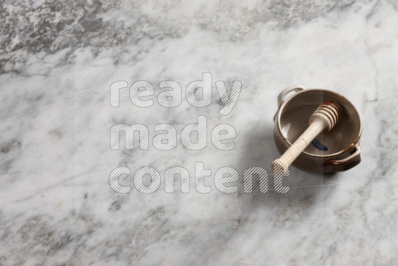 Multicolored pottery bowl with wooden honey dipper in it on grey marble background