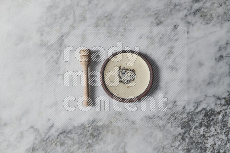 Decorative pottery plate with wooden honey dipper on the side on grey marble background