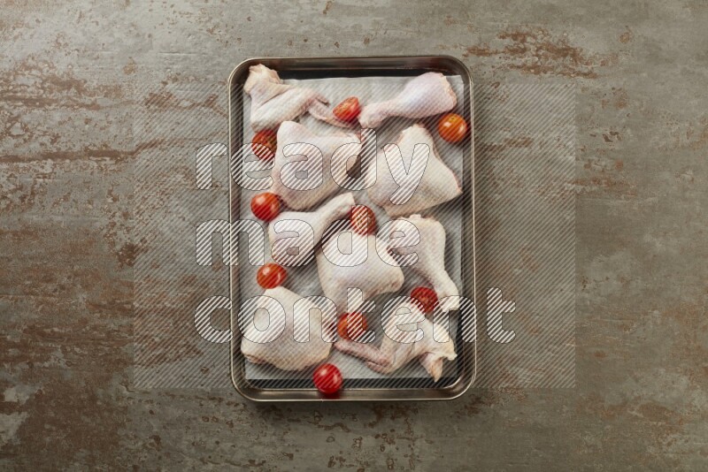 Mixed fresh chicken pieces in an oven tray on a textured rustic background