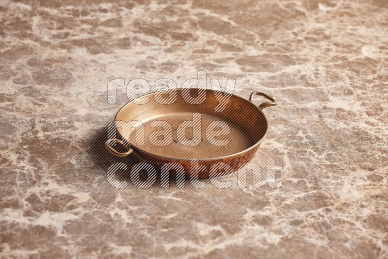 A small copper pan on beige marble background