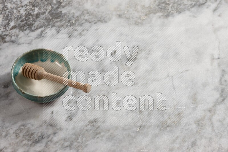 Multicolored pottery bowl with wooden honey dipper in it on grey marble background