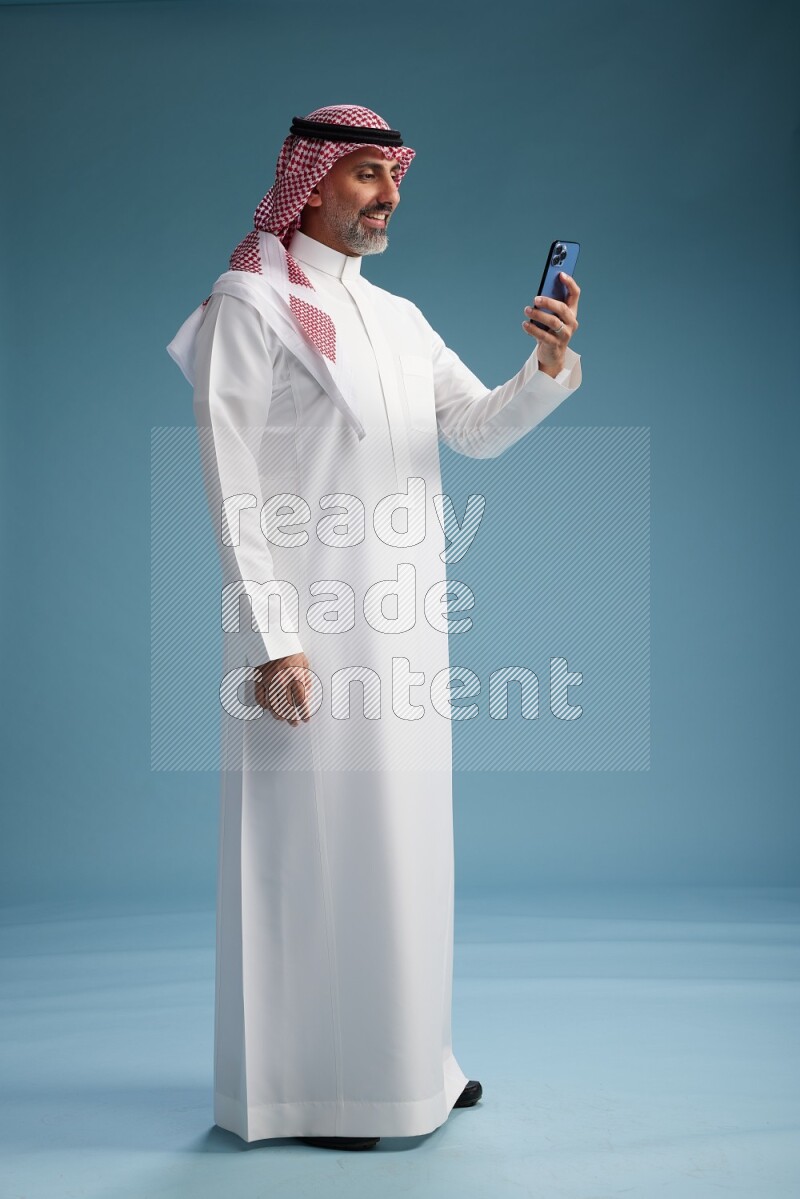 Saudi man wearing thob and shomagh texting on blue background