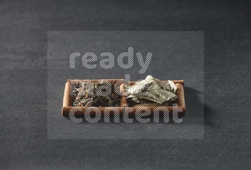 مربعان من أعواد القرفة ممتلئان بأوراق الغار والريحان المجفف علي خلفية سوداء