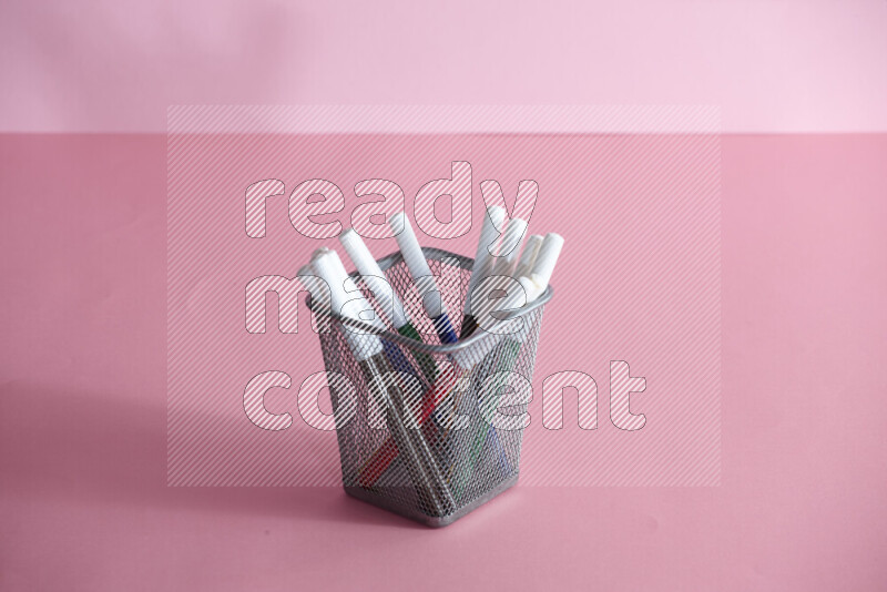 Pens, pencils and other different school supplies in a metal pen holder on rose background