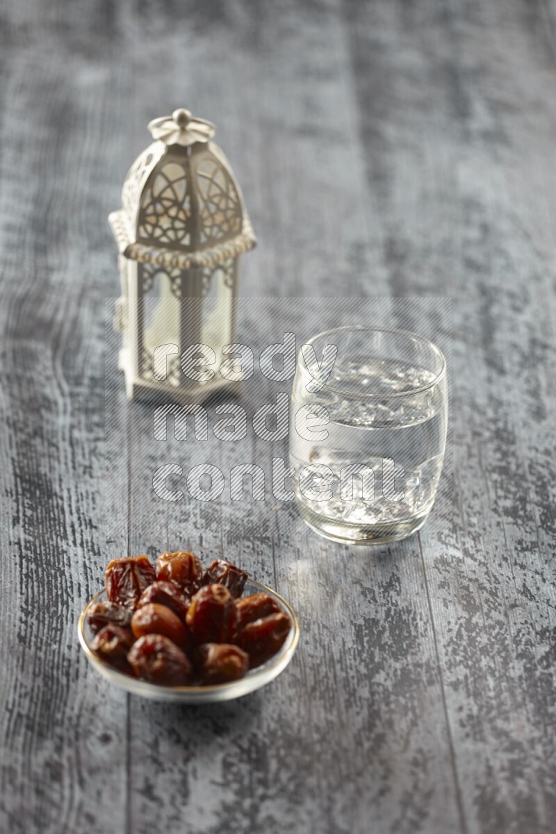 A white lantern with different drinks, dates, nuts, prayer beads and quran on grey wooden background