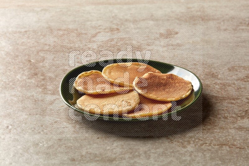 Five stacked plain mini pancakes in a green plate on beige background