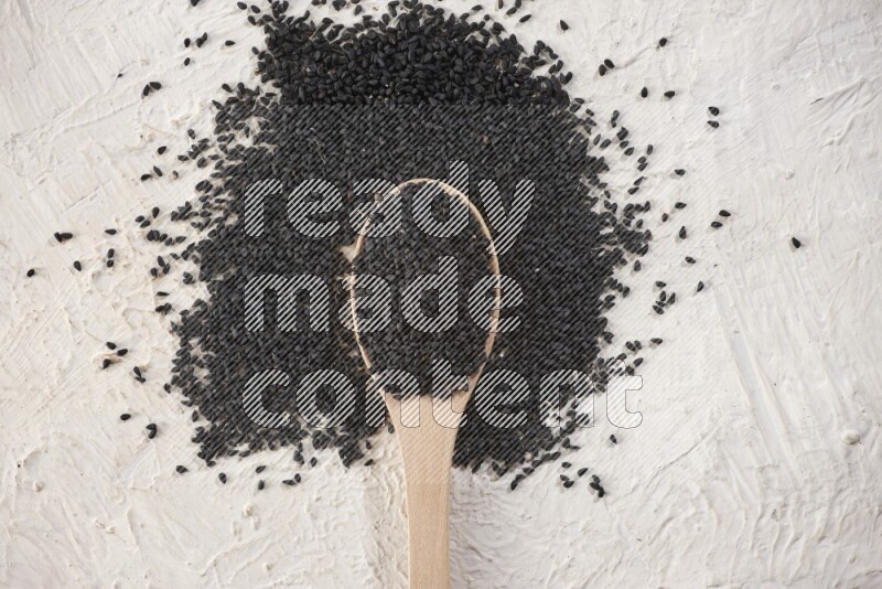 A wooden spoon full of black seeds on textured white flooring