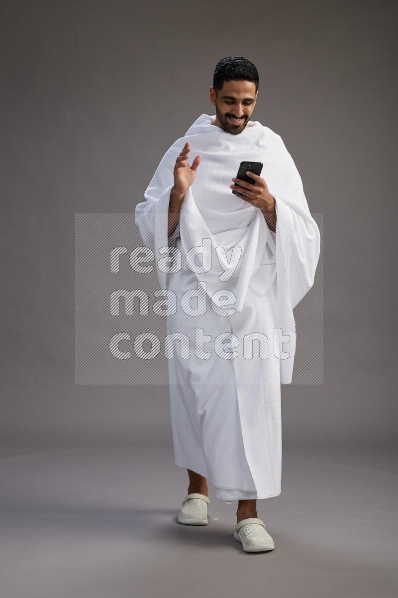 A man wearing Ehram Standing texting on phone on gray background
