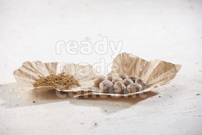 2 crumpled piece of paper full of nutmeg seeds and powder on a textured white flooring