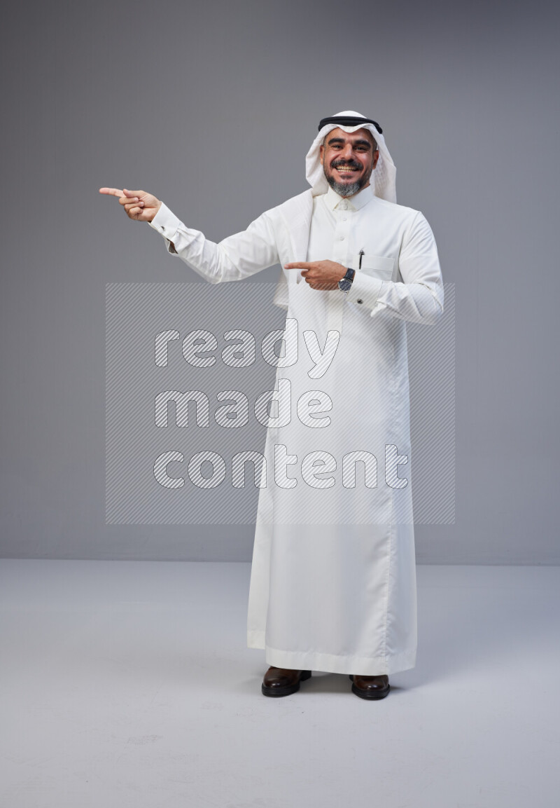 Saudi man Wearing Thob and white Shomag standing interacting with the camera on Gray background