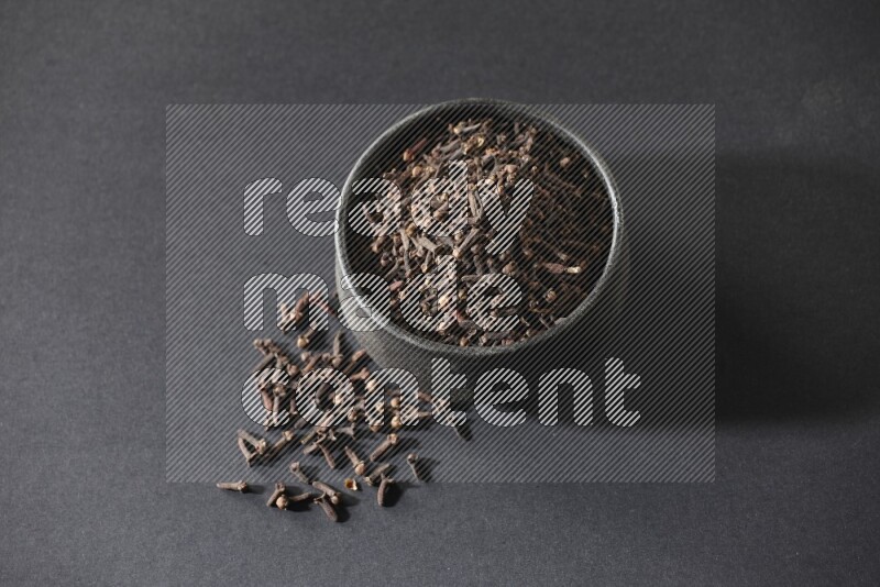 وعاء فخاري أسود ممتلئ بحبوب القرنفل علي خلفية سوداء