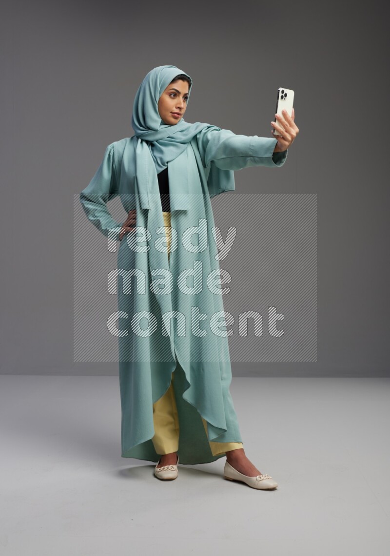 Saudi Woman wearing Abaya standing taking selfie on Gray background