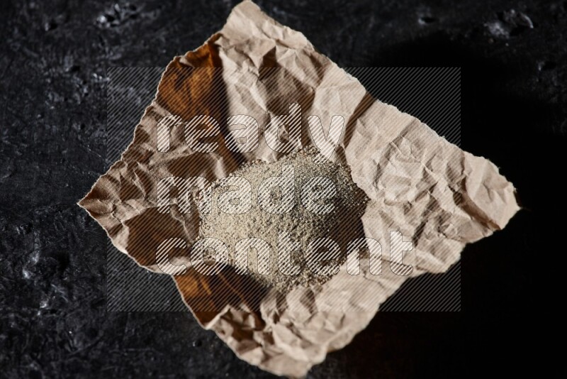 White pepper powder in a crumpled paper on textured black flooring