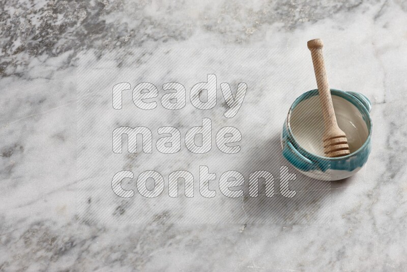 Multicolored pottery bowl with wooden honey dipper in it on grey marble background