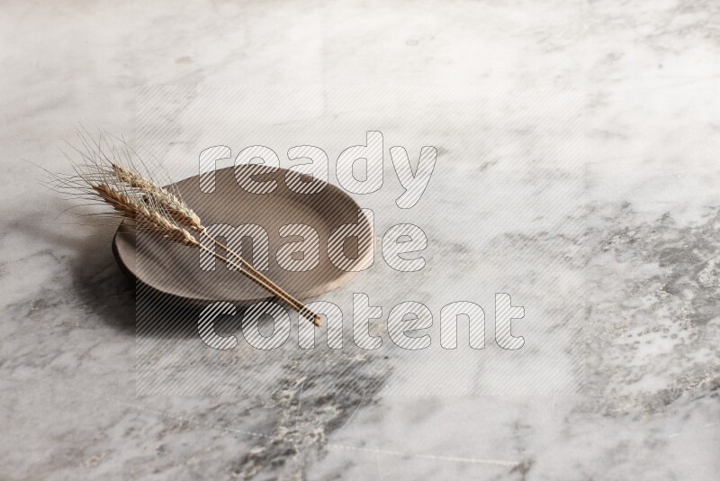 Wheat stalks on multicolored pottery plate on grey marble background
