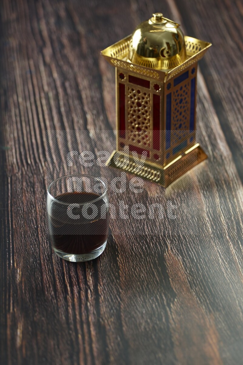 A golden lantern with different drinks, dates, nuts, prayer beads and quran on brown wooden background