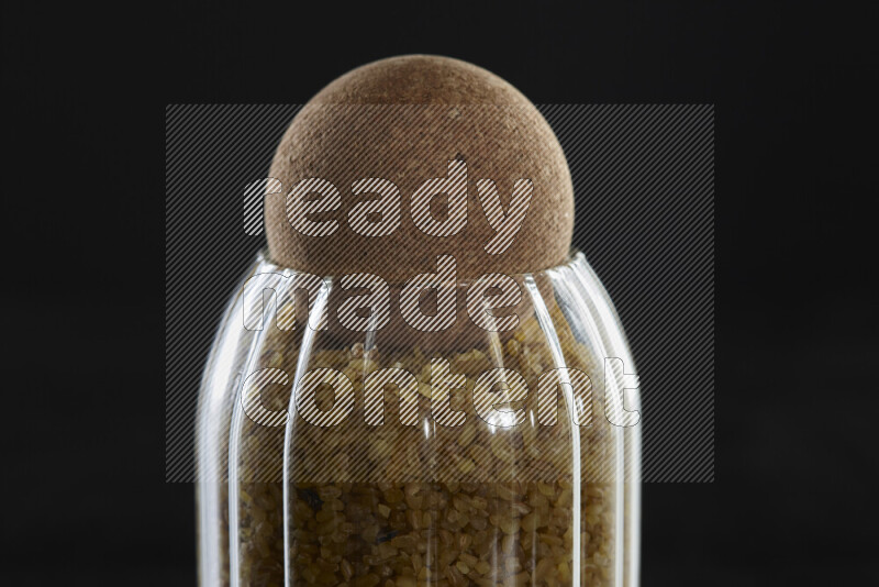 Coarse bulgur in a glass jar on black background