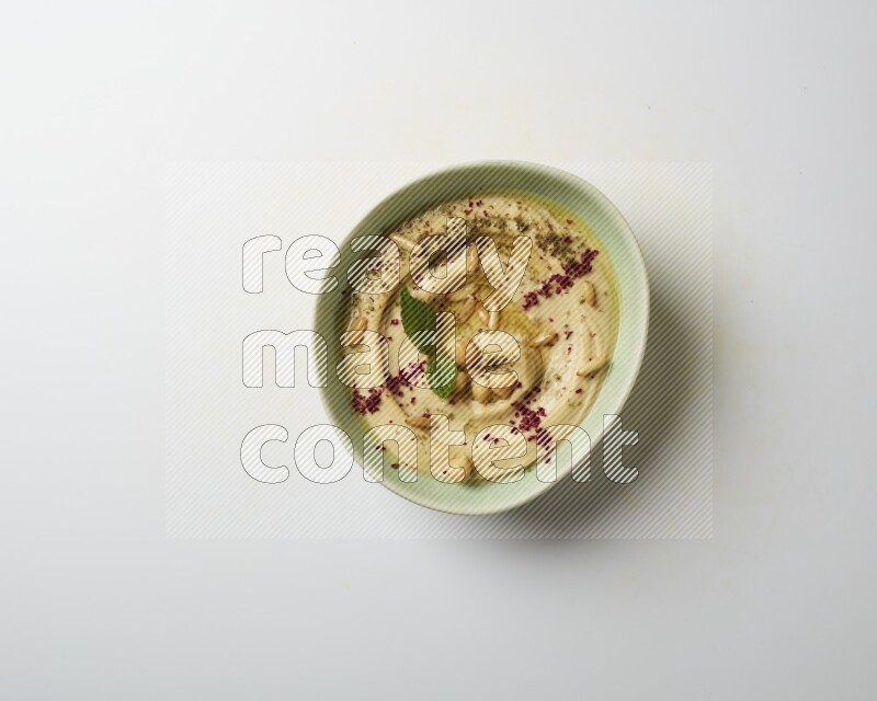 Hummus in a green plate garnished with zattar & sumak on a white background