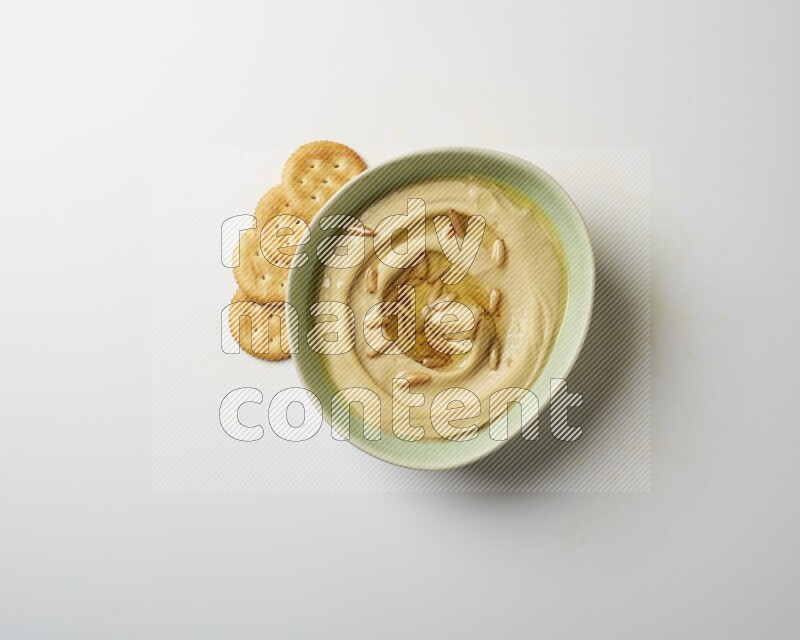 Hummus in a green plate garnished with pine nuts on a white background