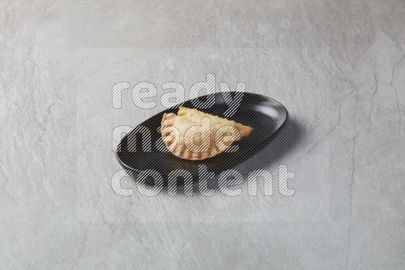 Two fried sambosas in an oval shaped black plate on a gray background