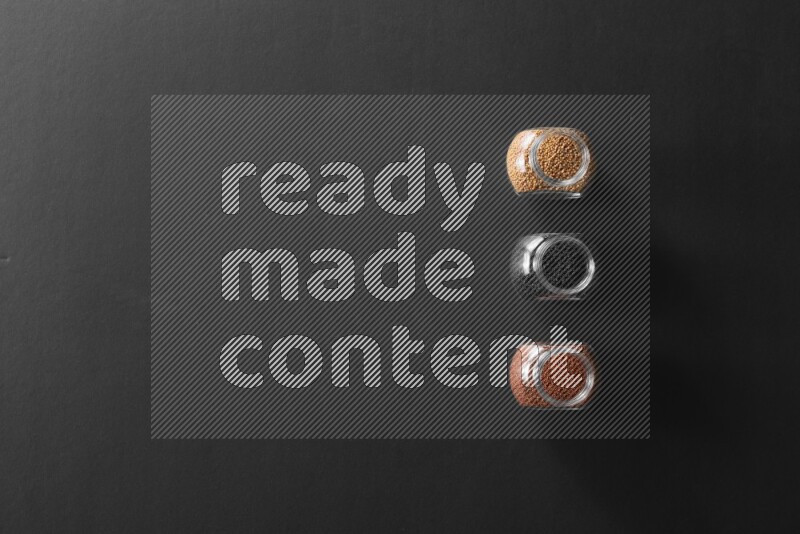 3 glass spice jars full of black seeds, mustard seeds and garden cress on black flooring