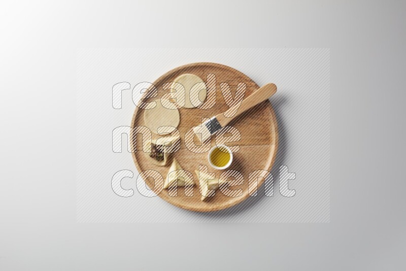 two closed sambosas and one open sambosa filled with meat while oil with oil brush aside in a wooden dish on a white background