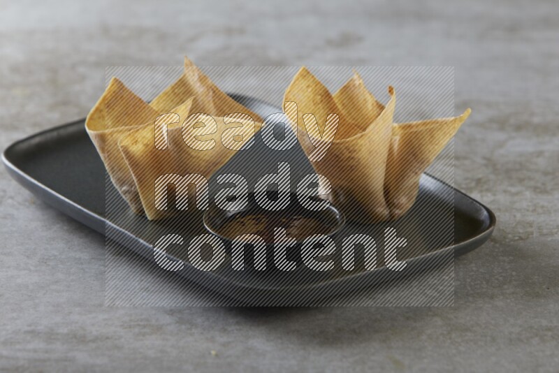 wonton cups with soy sauce ramkin on rectangle dark grey ceramic plate on grey textured counter top