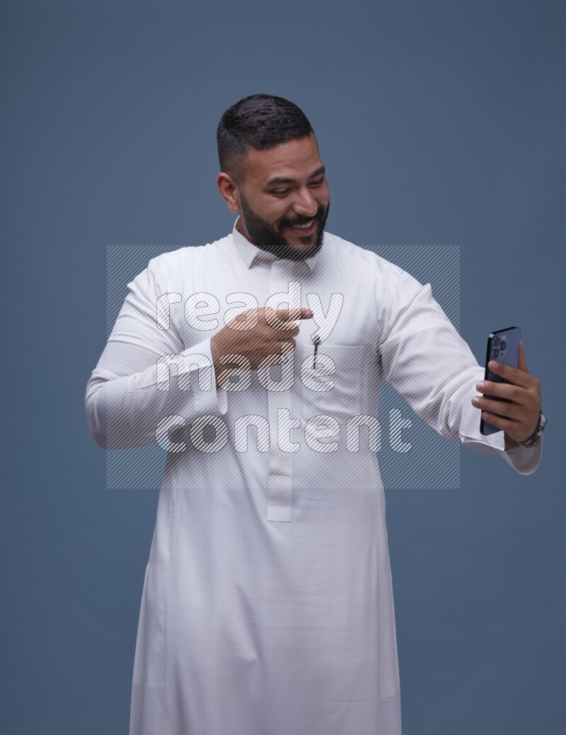 A Saudi man Taking A Selfie on Blue Background wearing Saudi Thob