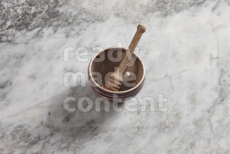 Multicolored pottery bowl with wooden honey dipper in it on grey marble background