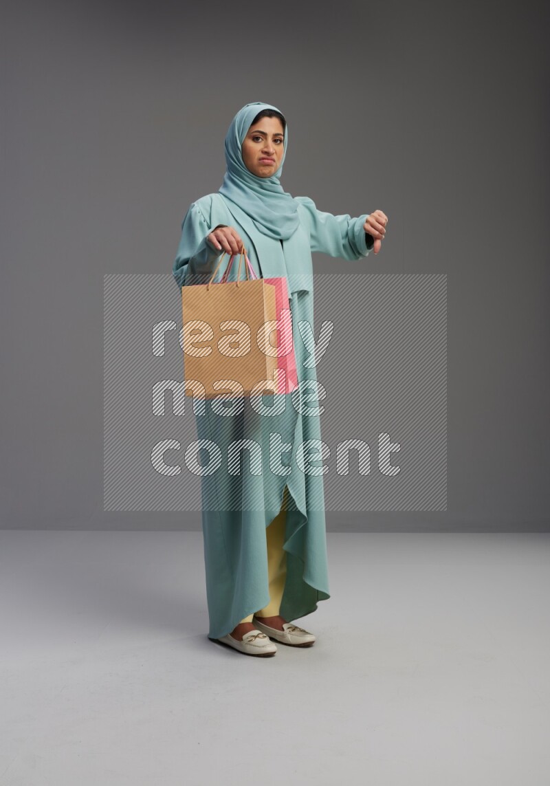 Saudi Woman wearing Abaya standing holding shopping bag on Gray background