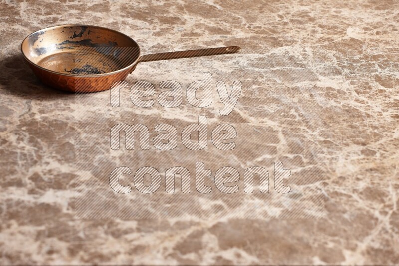 A small copper pan on beige marble background