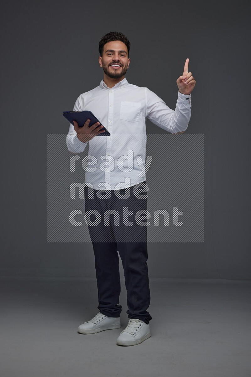 A man wearing smart casual standing and using his tablet and making multi hand gestures eye level on a gray background