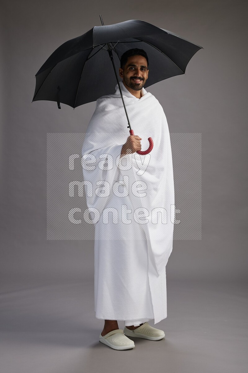 A man wearing Ehram Standing holding umbrella on gray background