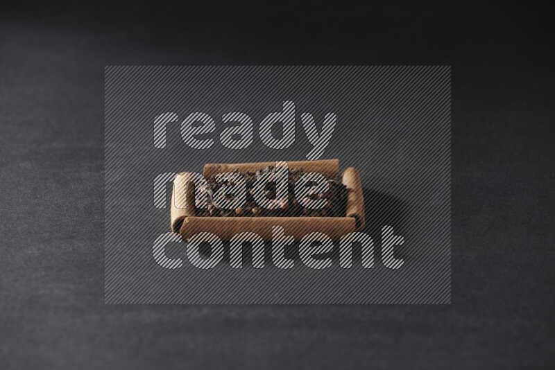 أربعة من أعواد القرفة مكونة شكل مربع بداخلها حبوب قرنفل علي خلفية سوداء