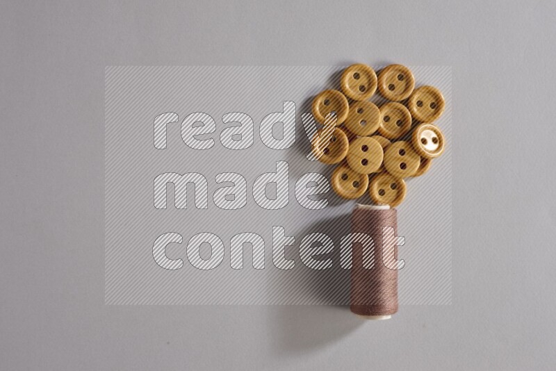 A brown sewing thread spool with colored buttons on grey background