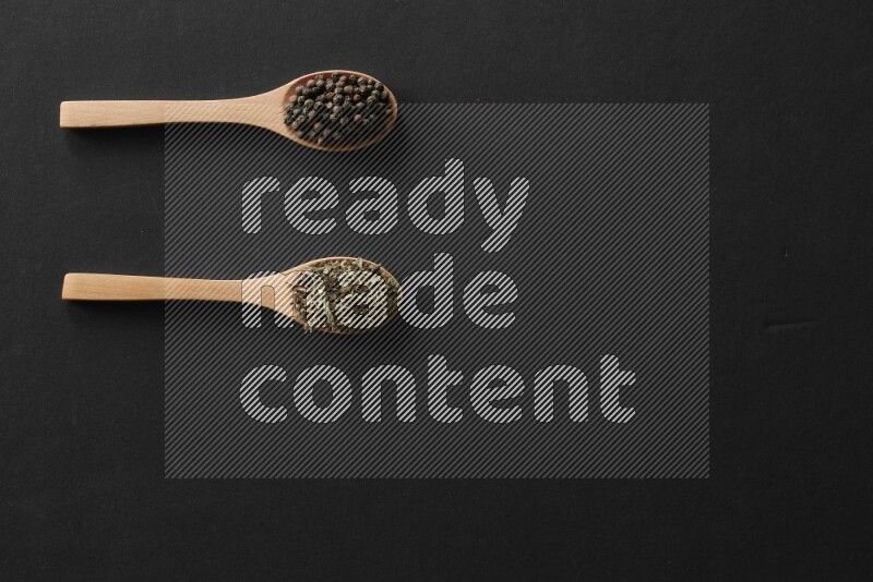 الفلفل الأبيض والقرنفل والهيل والملح والفلفل الأسود وريحان مجفف في معالق خشبية علي خلفية سوداء