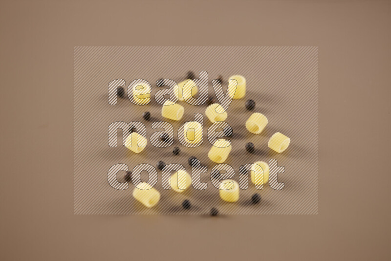 Raw pasta with different ingredients such as cherry tomatoes, garlic, onions, red chilis, black pepper, white pepper, bay laurel leaves, rosemary and cardamom on beige background