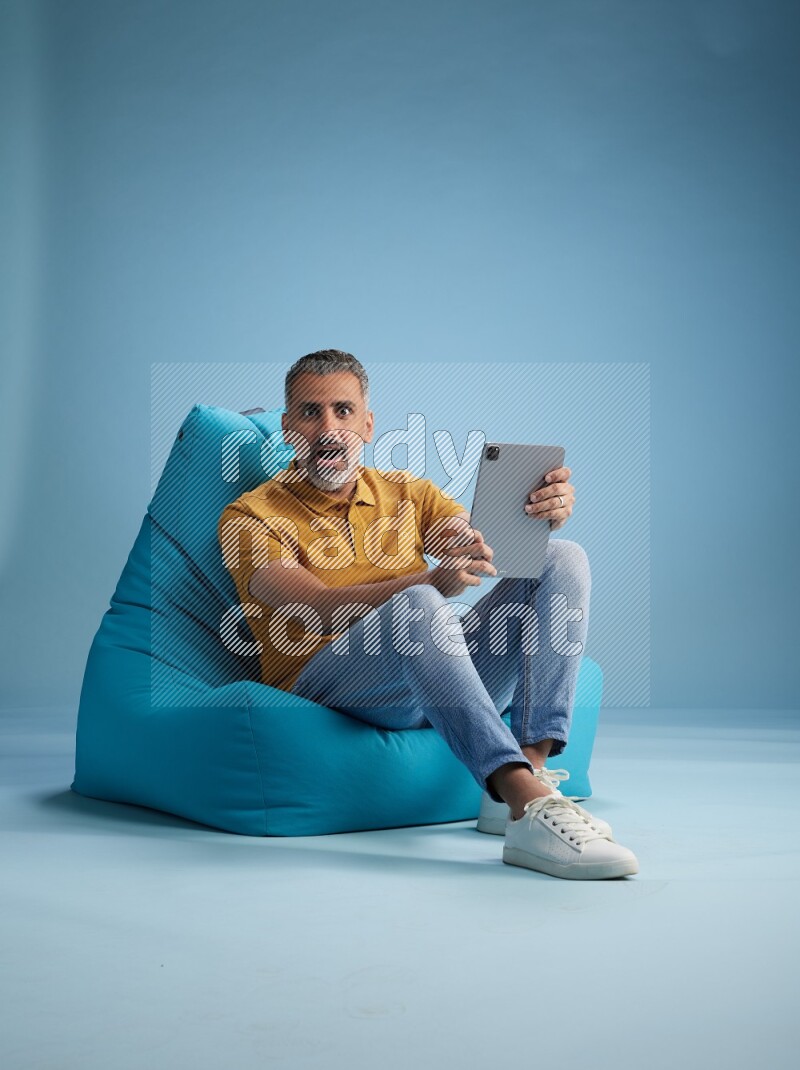 A man sitting on a blue beanbag and working on tablet