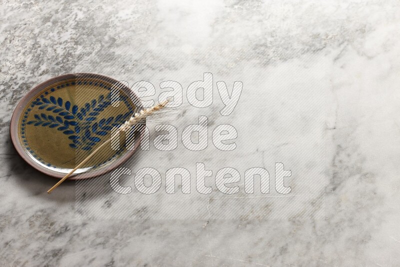 Wheat stalks on decorative pottery plate on grey marble background