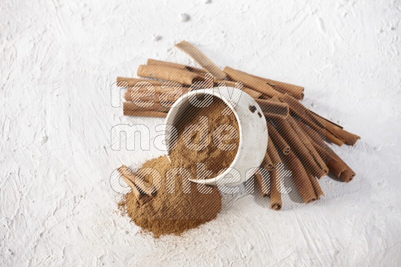 Ceramic beige bowl over filled with cinnamon powder and cinnamon sticks around the bowl on a textured white background in different angles