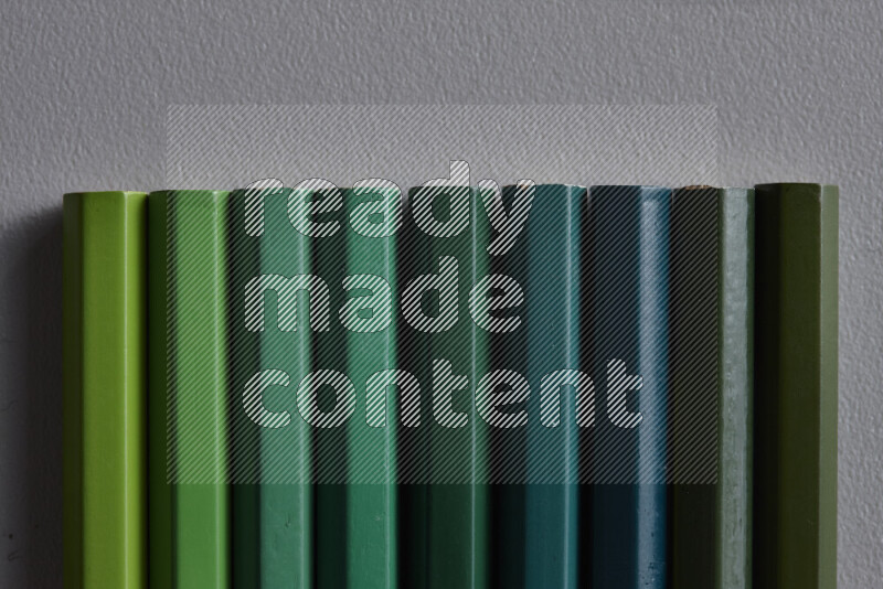 مجموعة من أقلام الرصاص الملونة مرتبة لتعرض تدرجا من الألوان الخضراء علي خلفية رمادية