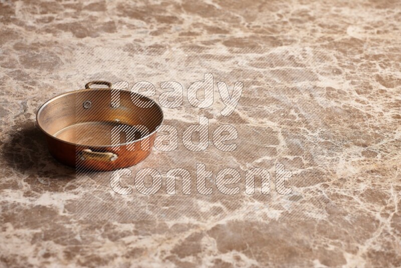 A small copper pan on beige marble background
