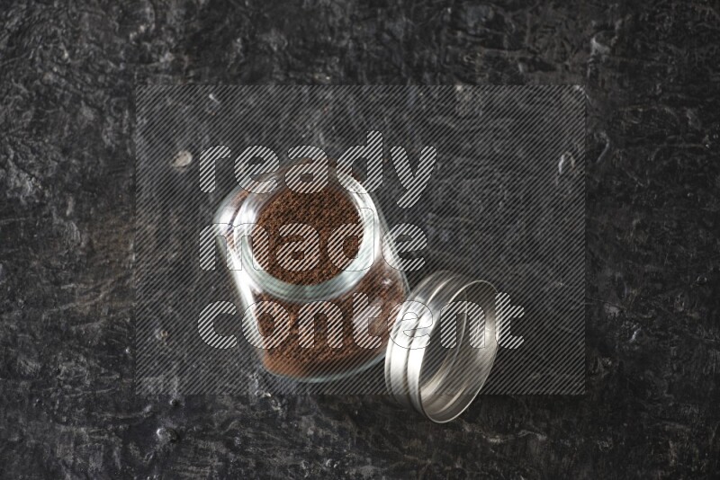 وعاء بهارات زجاجي ممتلئ ببودرة القرنفل على أرضية سوداء