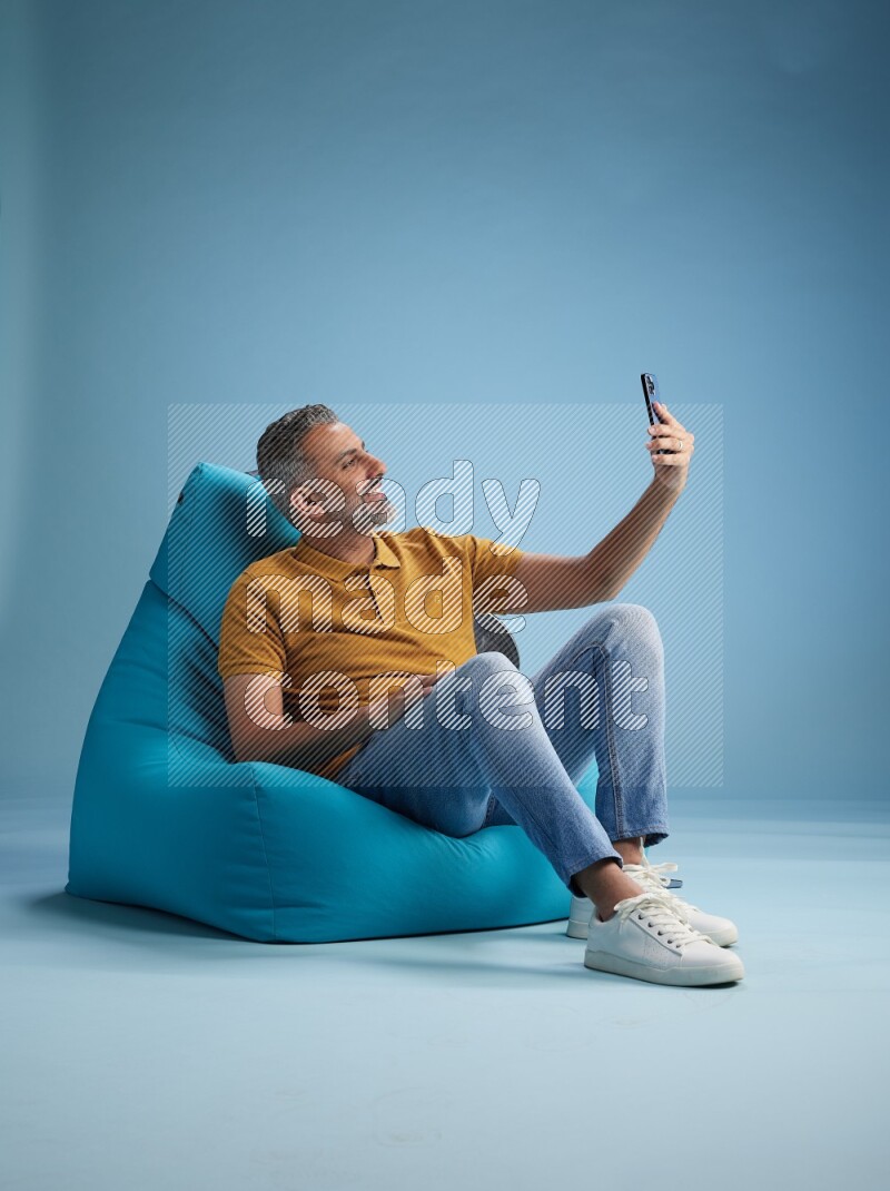 A man sitting on a blue beanbag and taking selfie